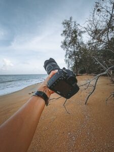 faceless photographer holding digital camera against sandy seashore